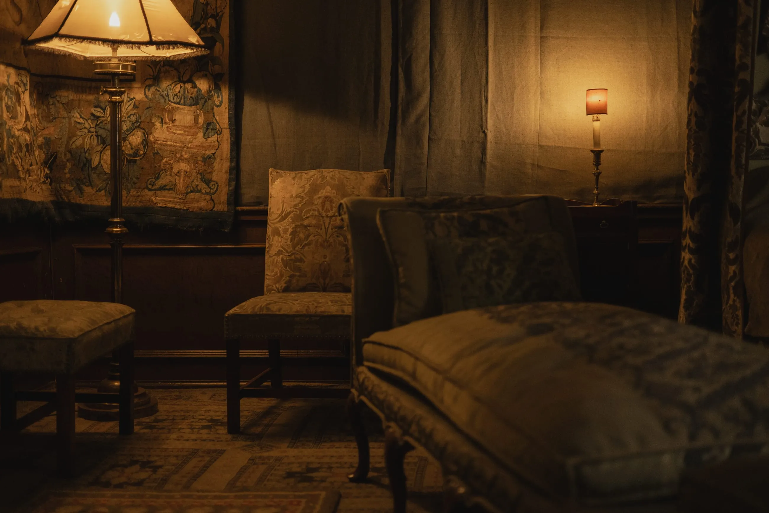 Lamp-lit bedroom with tapestries and an old armchair