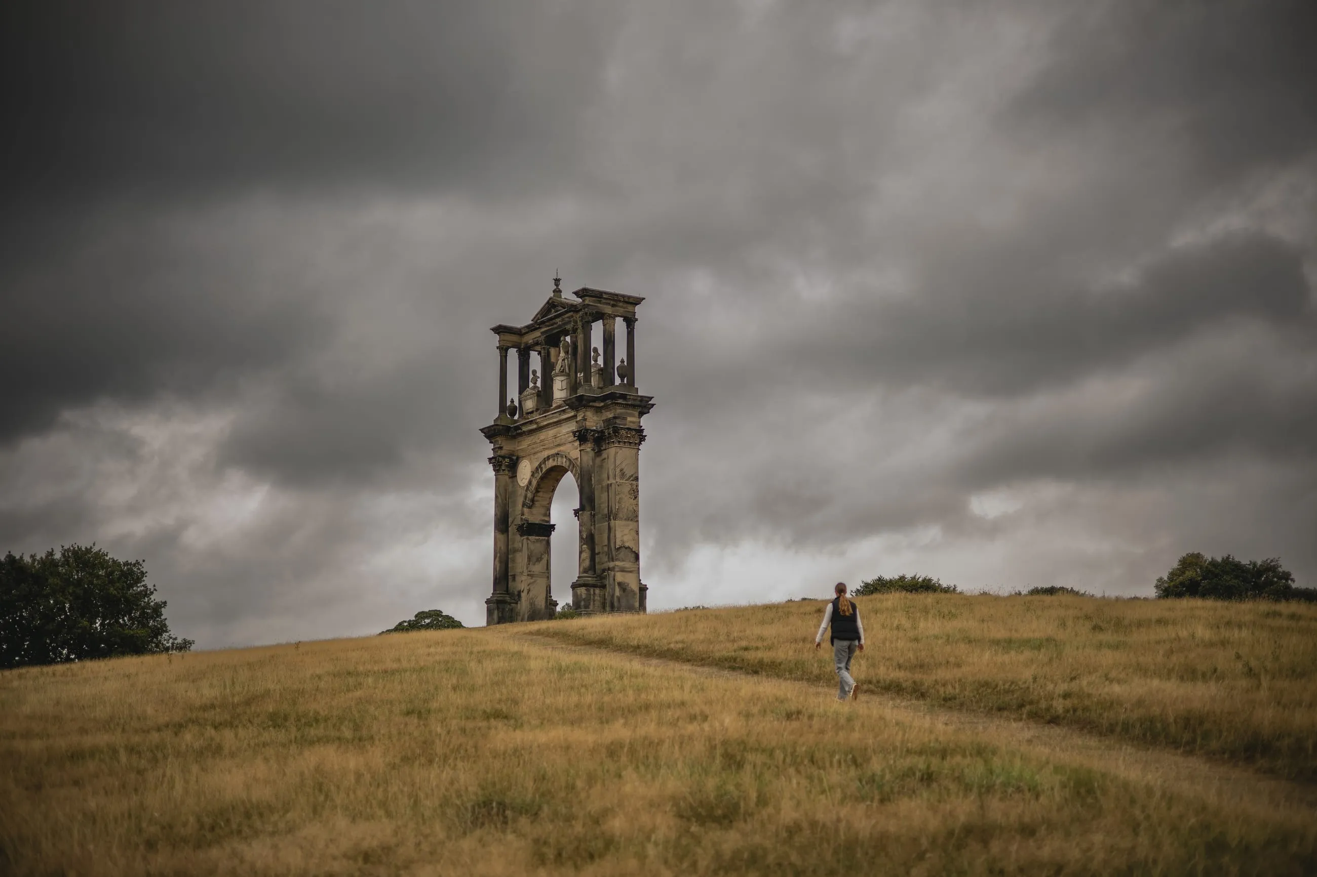 Lone figure walking towards a ruined arch on a hill
