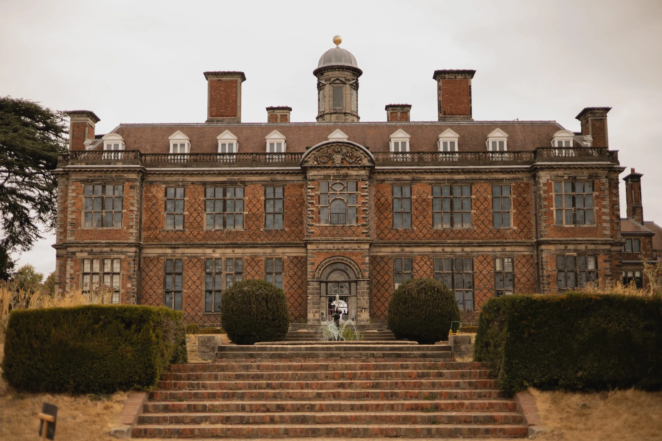 Red-brick Jacobean hall front with steps and topiary