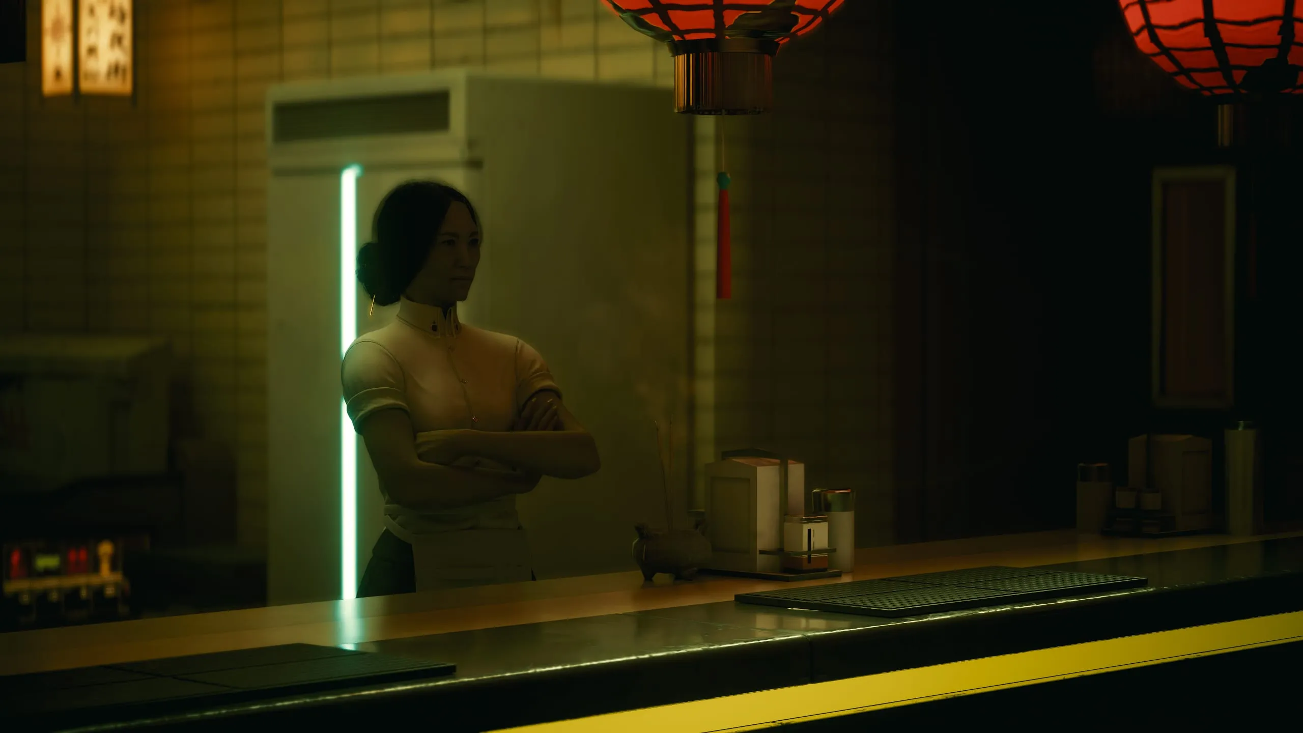 Waitress, arms folded, behind a noodle bar under lanterns