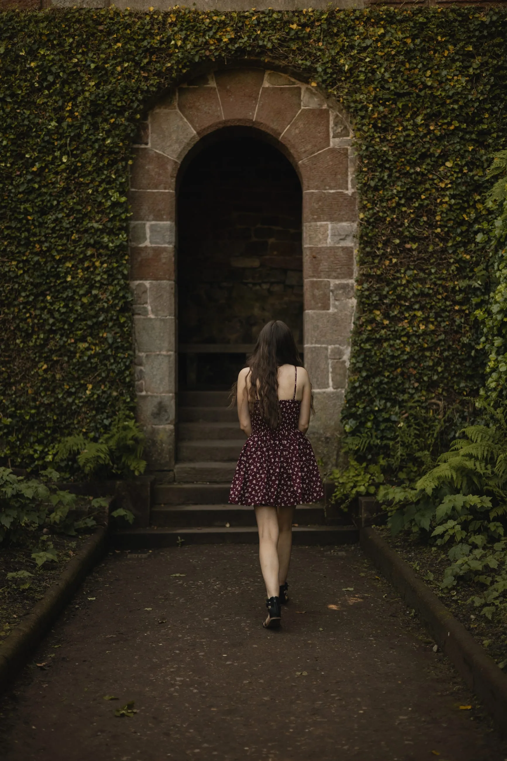 Woman climbing steps into a stone archway in ivy