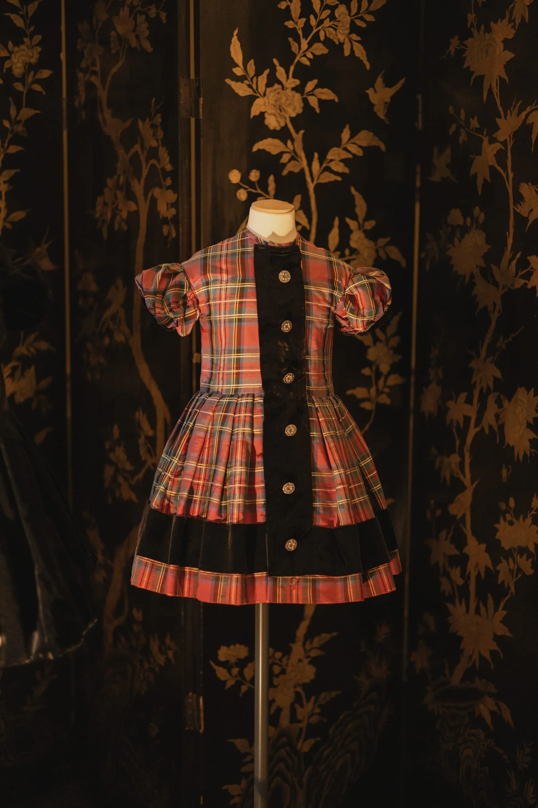 Tartan child's dress on display against dark wallpaper
