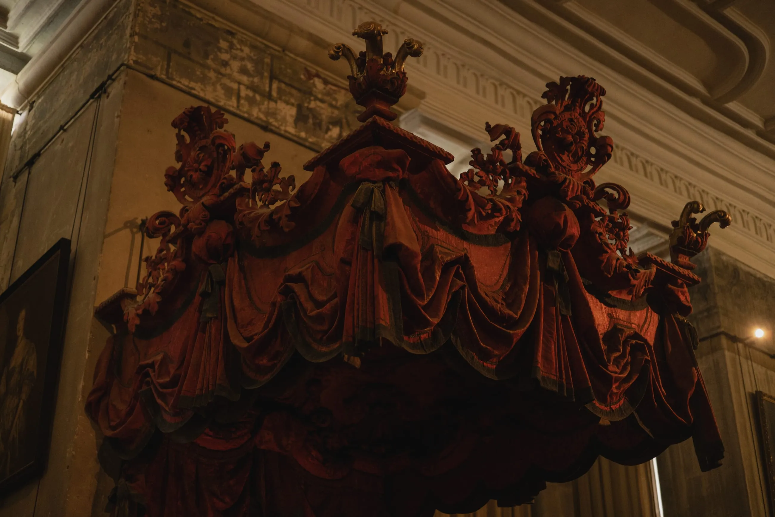 Carved red velvet bed canopy in a dim room