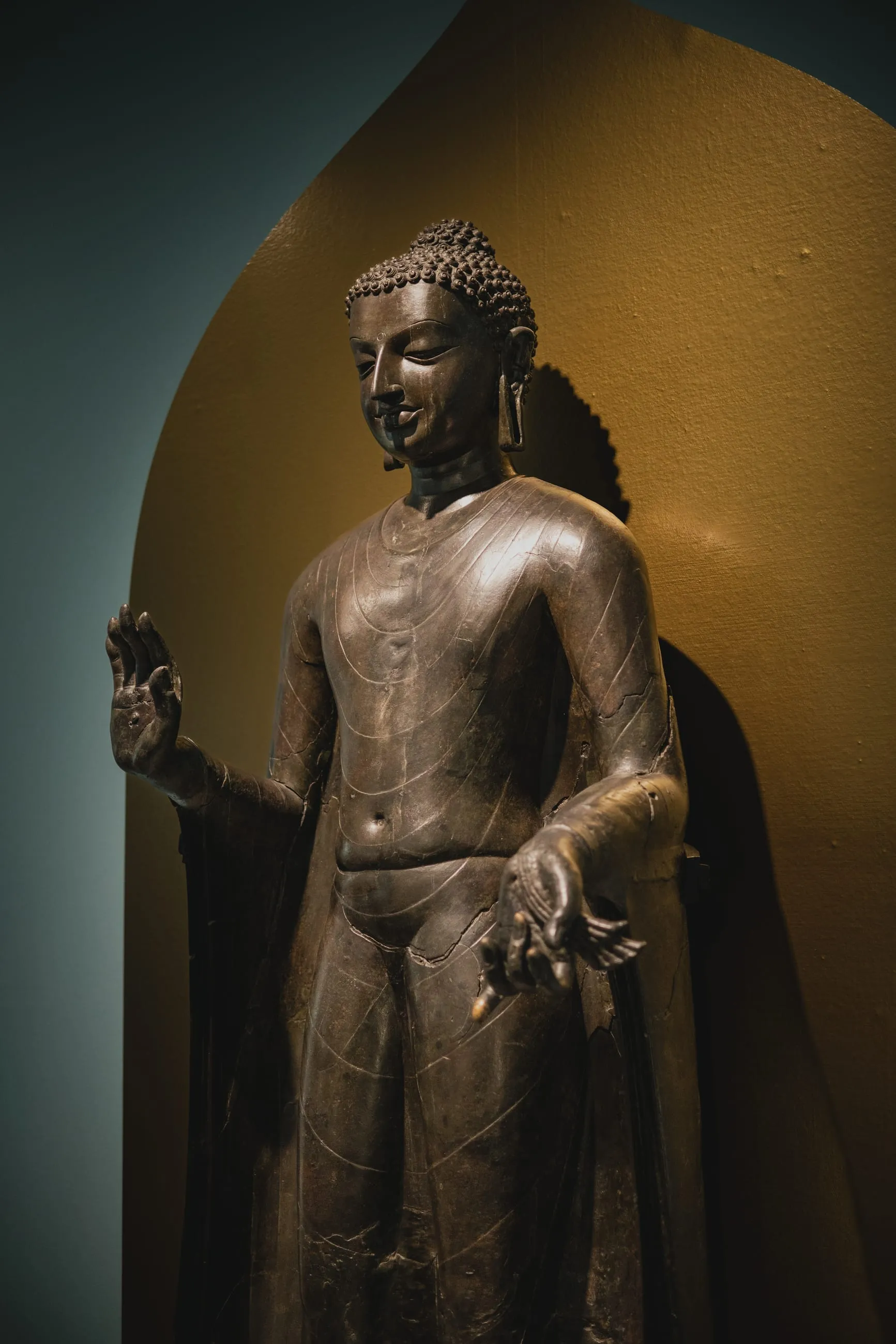 Bronze standing Buddha in a lit museum niche