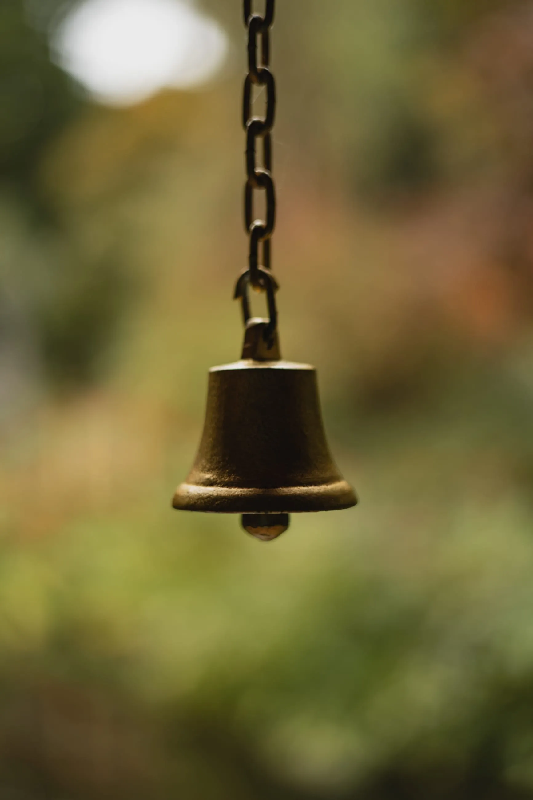 Brass bell hanging against blurred autumn colour