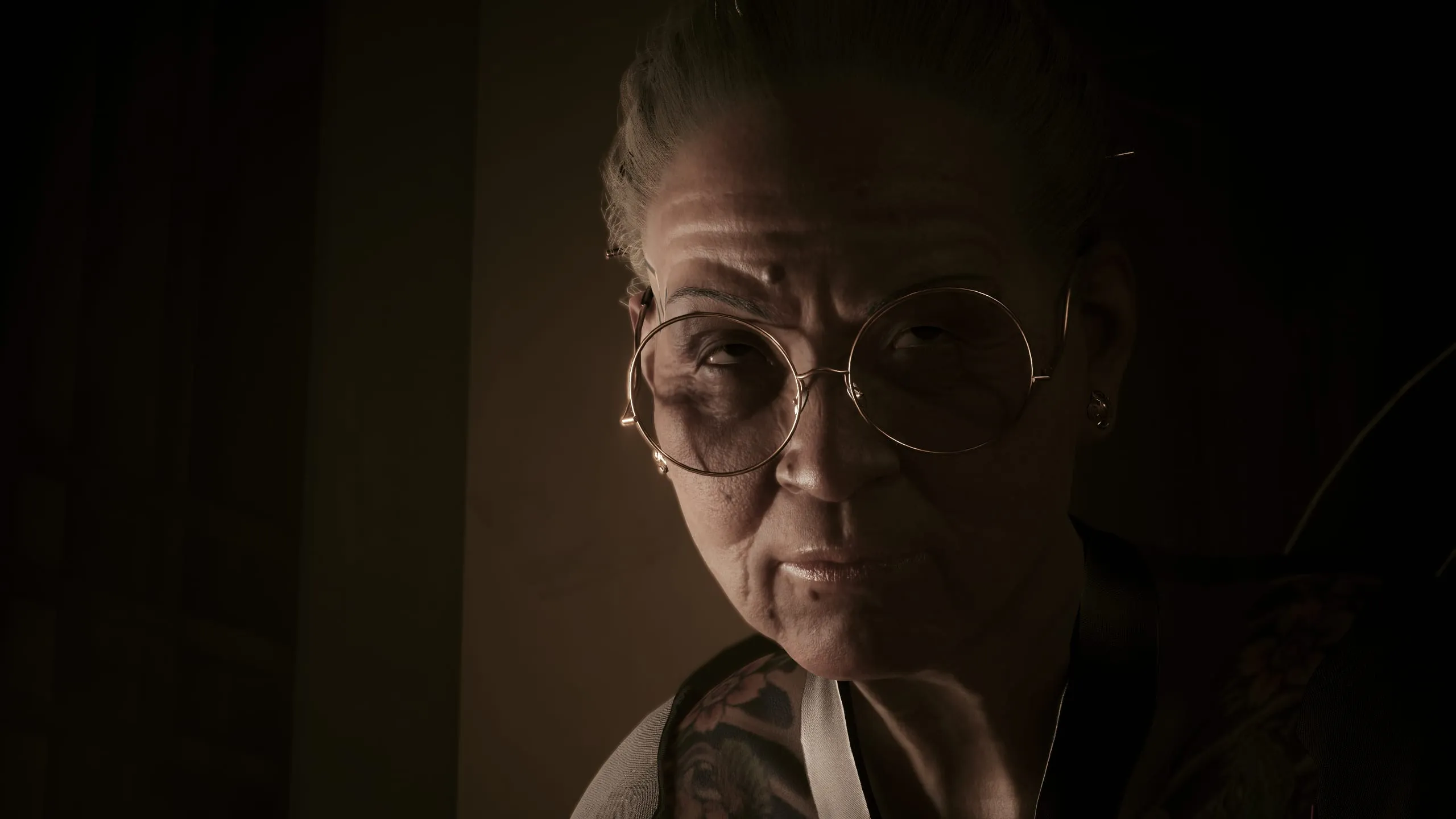 Older woman in large glasses, lit softly from the side