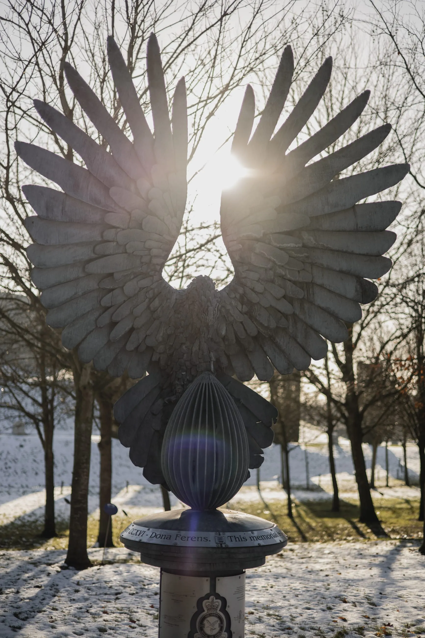 Winged steel sculpture backlit by low winter sun