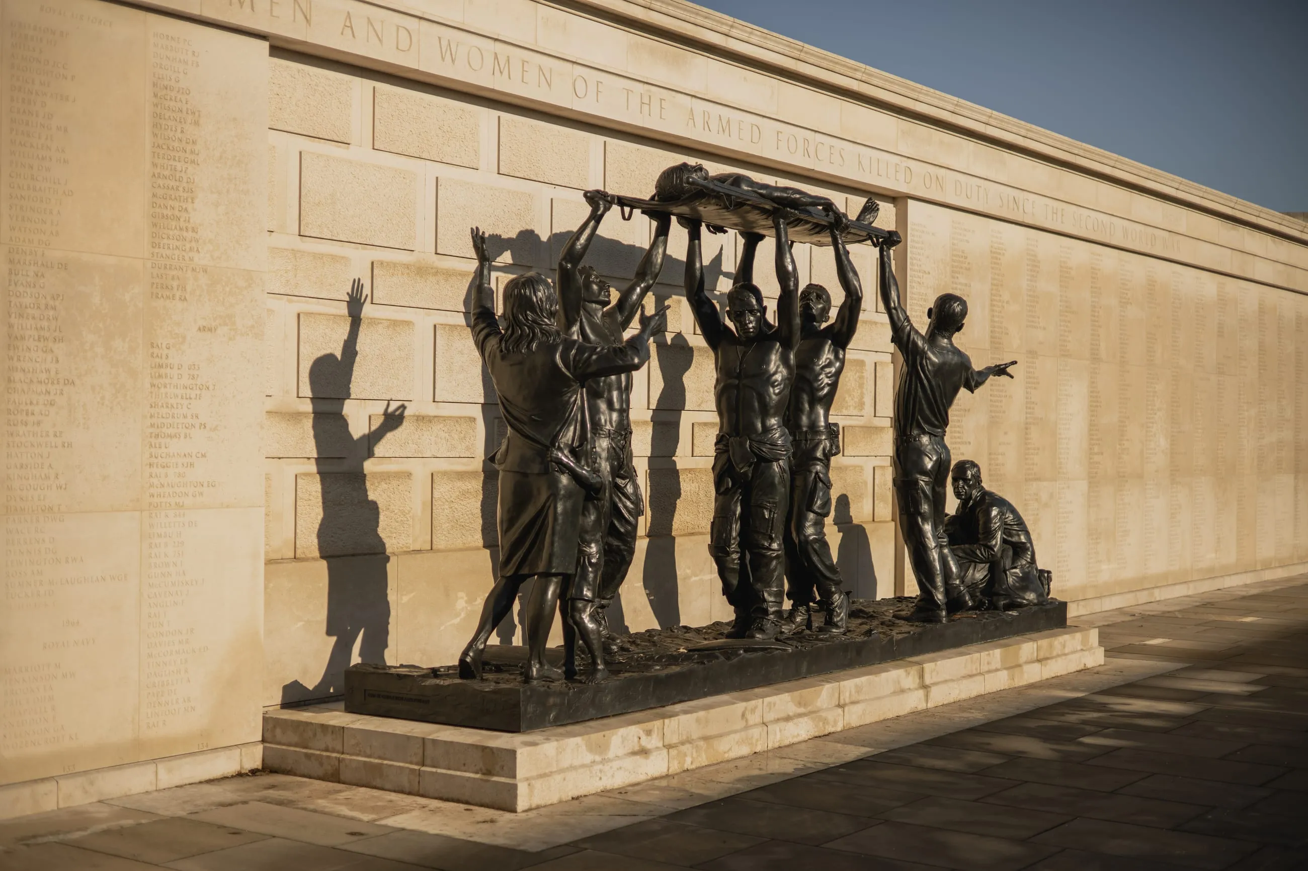 Bronze figures carrying a body, long shadows on stone