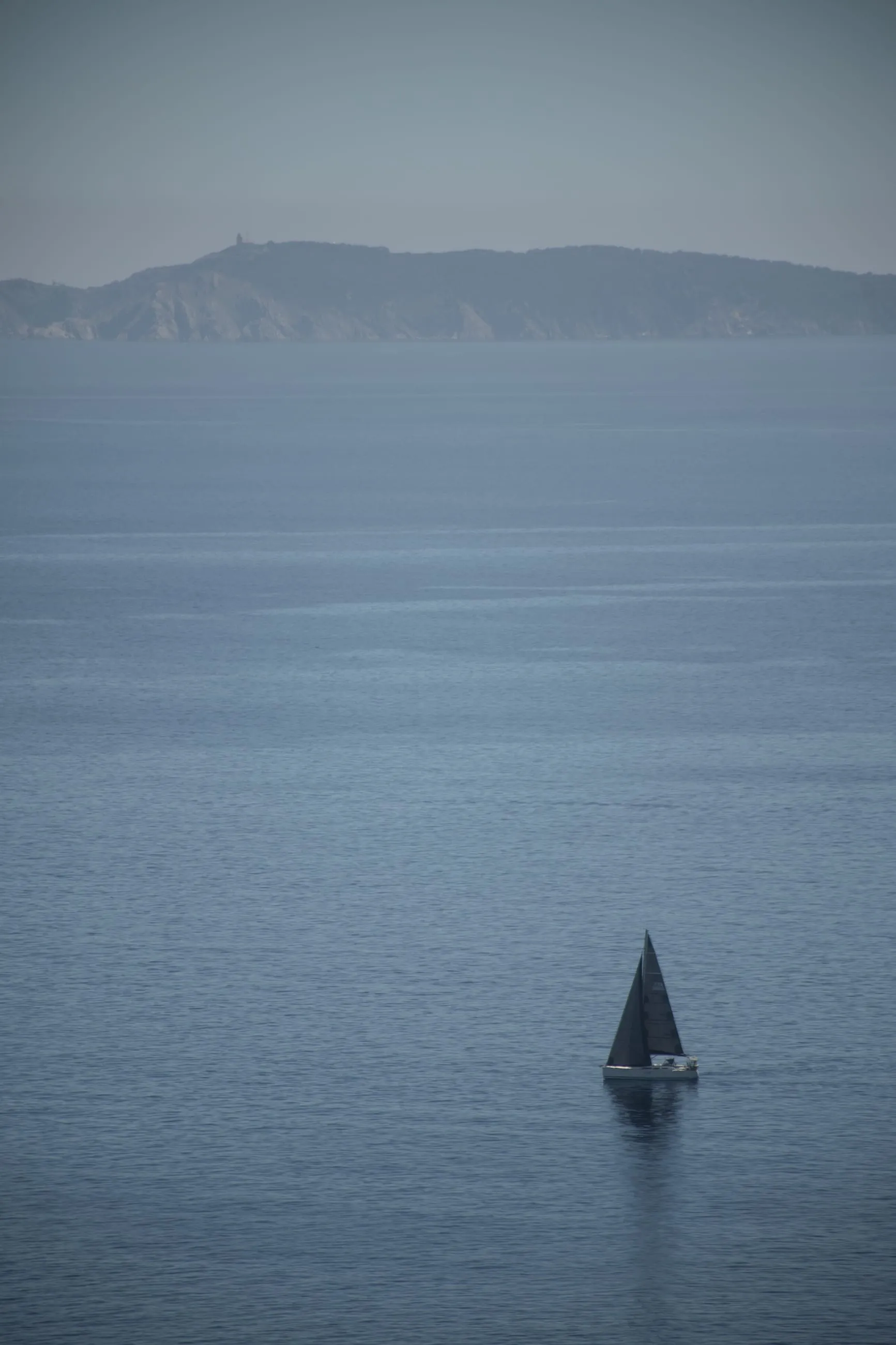 Small sailboat alone on a hazy blue sea